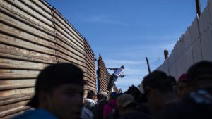 A Central American migrant climbs the border fence between Mexico and