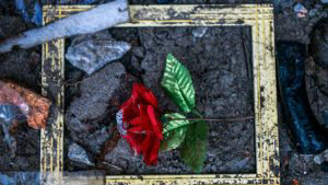 An artificial rose is seen on the floor outside a collapsed home in R