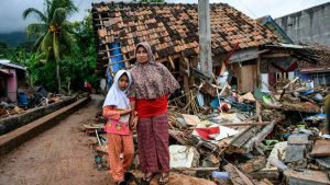 TOPSHOT - A girl holds her mother's hand in front of a collapsed hous