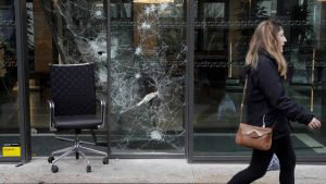 A woman walks along a broken window of a company on December 2