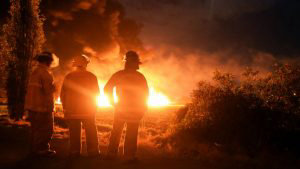 Firefighters stand at the scene of a massive blaze trigerred by a lea