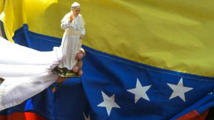 A faithful holds a souvenir doll of Pope Francis next to a Venezuelan