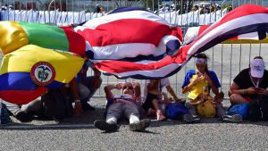 Pilgrims rest under flags as they wait for the arrival of Pope Franci