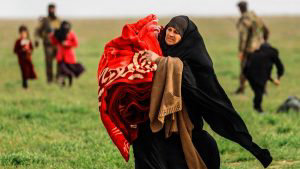 A woman carries a blanket as people queue at a scanning area for thos