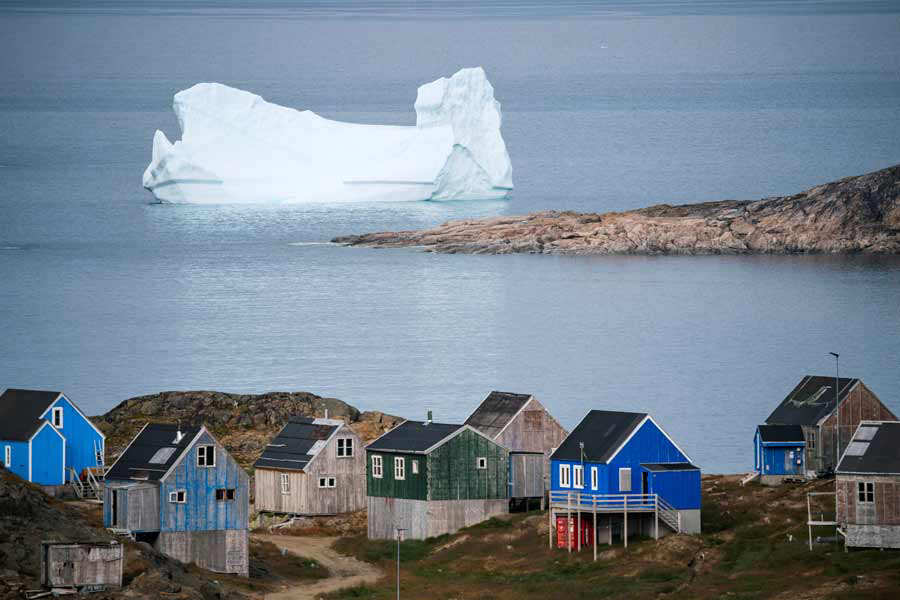 Icebergs flotan cerca de la costa detrás de coloridas casas en Kulusuk, un asentamiento en el municipio Sermersooq, en la costa sureste de Groenlandia. Foto AFP/ Jonathan NACKSTRAND 