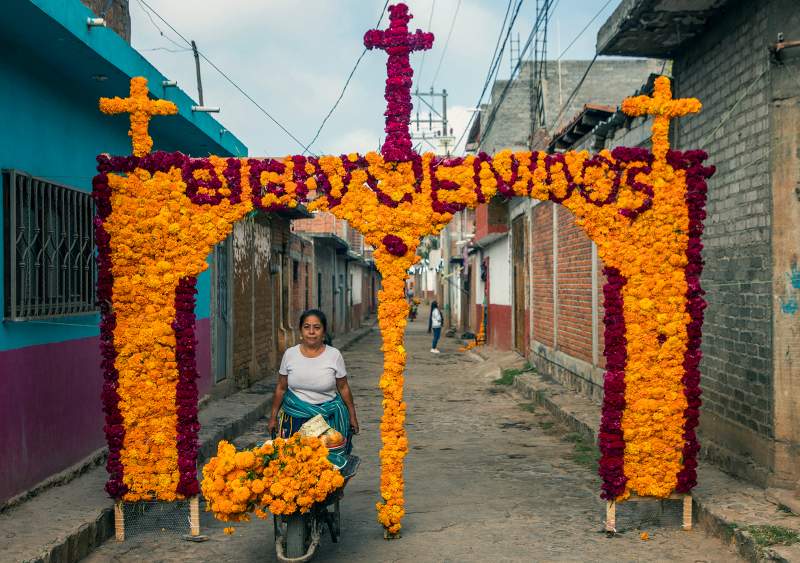 Un familiar de María Salud Ramírez Caballero, conocida como Mamá Coco, decora un arco con flores en la calle donde vivía para recibir la visita de turistas en Santa Fe de la Laguna. Foto: ENRIQUE CASTRO / AFP