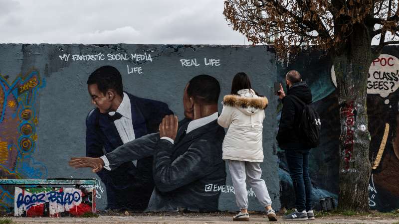 Una pareja en Berlín, Alemania, toma fotos de un mural del artista callejero Eme Freethinker, que muestra la imagen del actor estadounidense Will Smith (derecha) abofeteando al comediante Chris Rock durante la ceremonia de los Oscar. Foto: archivo / AFP