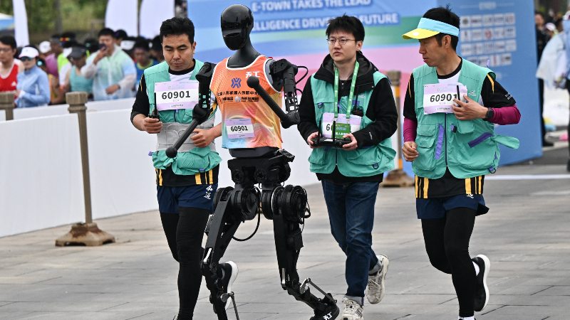Un robot y sus ingenieros corren la media maratón de robots humanoides en Pekín el 19 de abril de 2025.