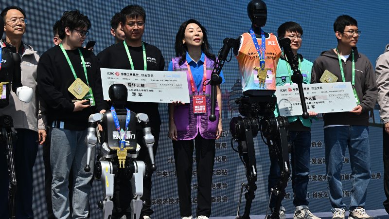 Robots e ingenieros asisten a la ceremonia de premiación tras la media maratón de robots humanoides en Pekín el 19 de abril de 2025.