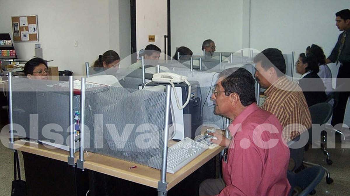 Grupo de personas sentadas en módulos individuales navegando por internet en un cibercafé salvadoreño.