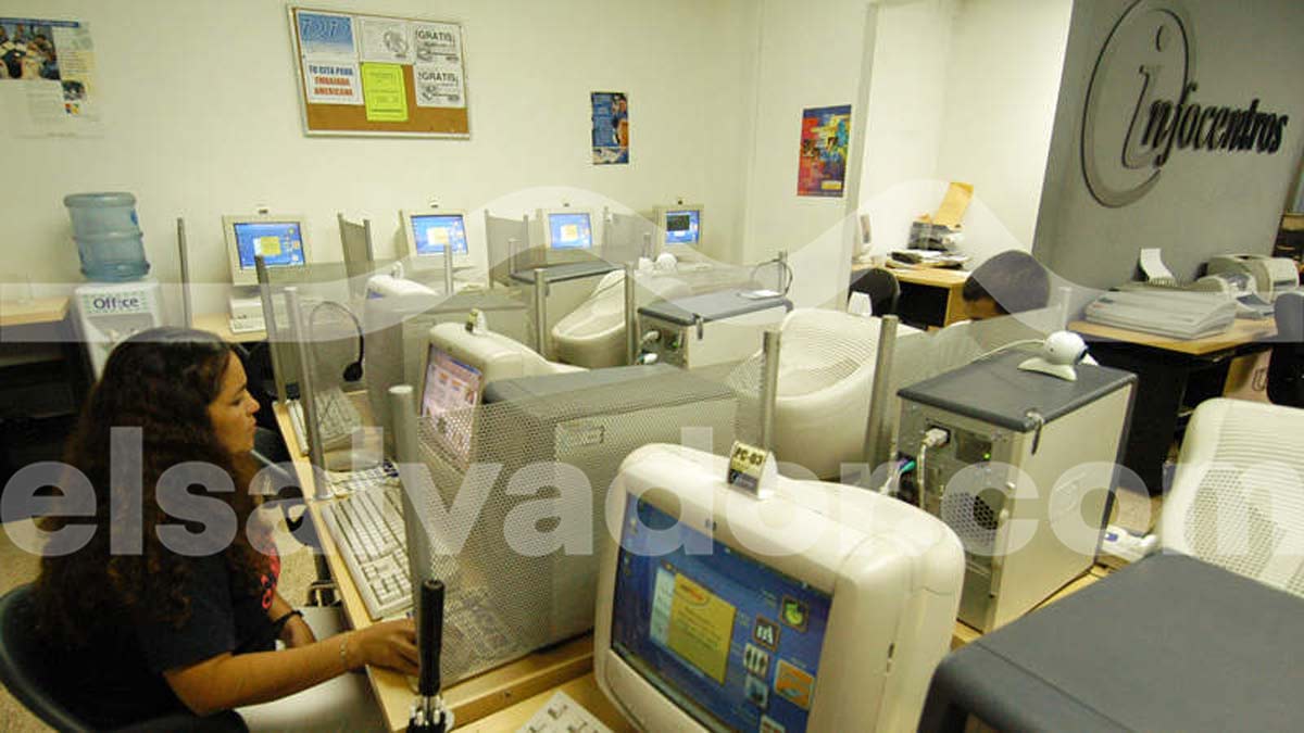 Vista interior de un Infocentro en El Salvador con filas de computadoras CRT con monitores blancos y usuarios navegando en internet.
