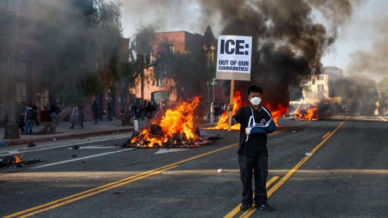  Un activista sostiene un cartel mientras se incendian vehículos durante las protestas provocadas por las redadas migratorias en Los Ángeles. EFE/EPA/ALLISON DINNER
