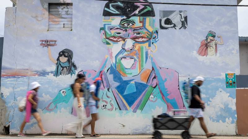 Personas camino a la playa pasan junto a un mural del cantante puertorriqueño Bad Bunny en Vega Baja, Puerto Rico, su municipio natal, el 13 de julio de 2025. / 