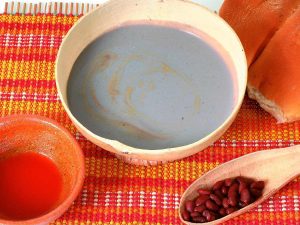 Atol shuco, bebida ancestral salvadoreña a base de maíz fermentado y frijol, servida con pan francés y chile.
