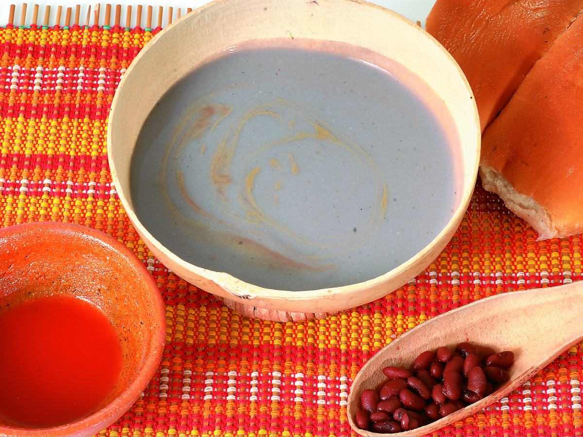 Atol shuco, bebida ancestral salvadoreña a base de maíz fermentado y frijol, servida con pan francés y chile.