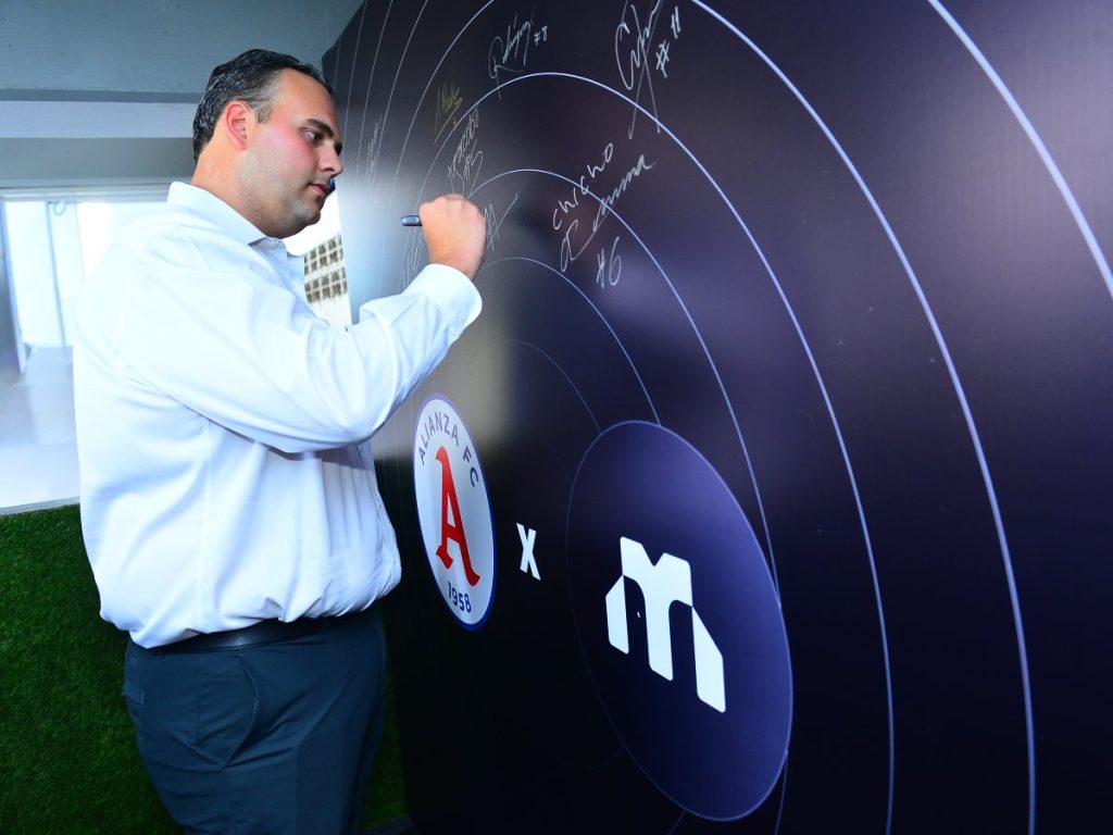 CEO de Monetae estampa su firma en el panel de alianzas estratégicas junto al logo de Alianza FC, oficializando el patrocinio.