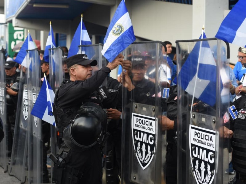 Elementos de la Policía Nacional Civil colocan banderas de El Salvador en sus escudos, sumándose al ambiente de unidad y orgullo nacional en la previa del partido.