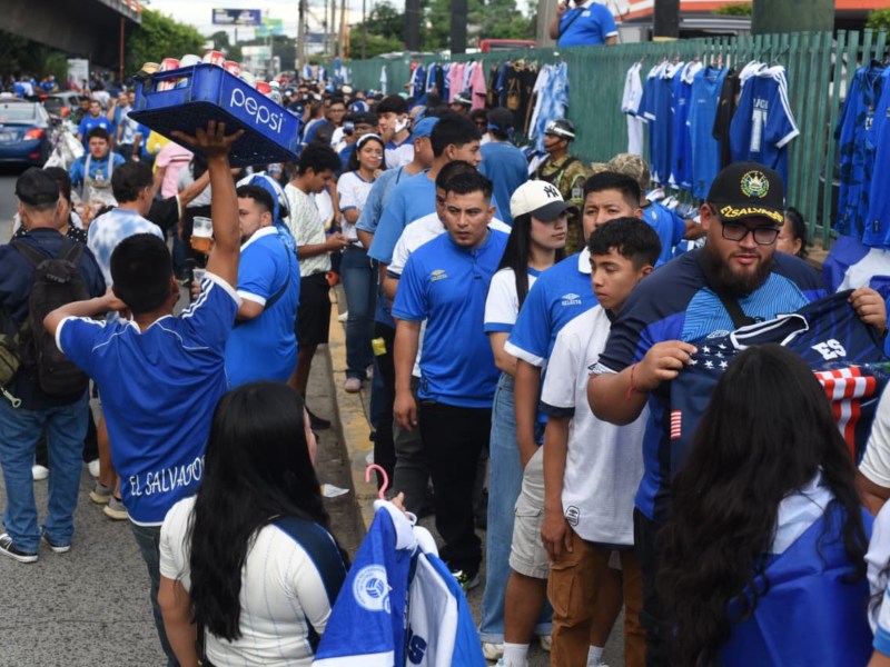 Aficionados salvadoreños hacen fila para ingresar al estadio, bajo la atenta vigilancia de autoridades, listos para apoyar a la Selecta con orgullo azul y blanco.
