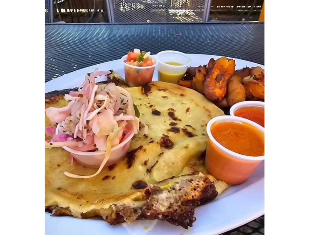 Las pupusas de Monse, servidas con curtido, salsa y plátanos fritos, combinan tradición y sabor casero salvadoreño.