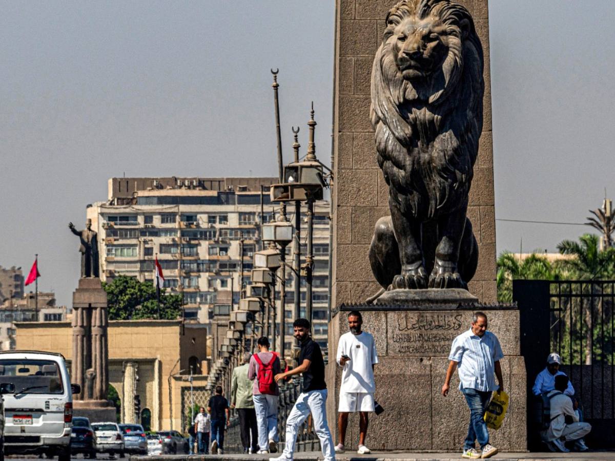 Personas caminan junto a una de las cuatro estatuas de leones de bronce al final del emblemático puente Qasr el-Nil, que conecta la plaza Tahrir, en el centro de El Cairo, con la isla de Zamalek (al fondo), el 6 de octubre de 2025. Delegaciones de Hamás, Israel y Estados Unidos se reunirán ese día en Egipto para dialogar, mientras el presidente Donald Trump insta a avanzar “rápido” para poner fin a casi dos años de guerra en Gaza. Foto/AFP