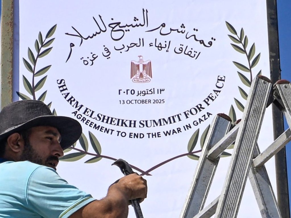 Un trabajador municipal coloca un cartel en Sharm el Sheij, mientras la ciudad turística egipcia se prepara para acoger la cumbre por la paz en Gaza impulsada por Estados Unidos, el 12 de octubre de 2025. Foto/ AFP