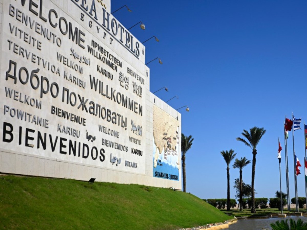 Un mural de bienvenida y Banderas de los países participantes en la cumbre por la paz en Gaza, impulsada por Estados Unidos, ondean en la ciudad turística egipcia de Sharm el Sheij, a orillas del mar Rojo, el 12 de octubre de 2025. Foto/ AFP