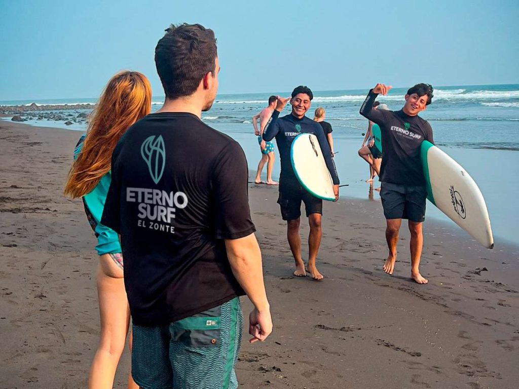 Jóvenes instructores de Eterno Surf regresan de una clase, fomentando el trabajo en equipo y el espíritu comunitario.