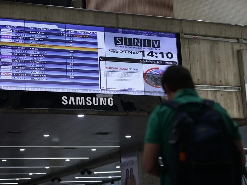 Fotografía de una persona caminando junto a una pantalla con la programación de vuelos, en el Aeropuerto Internacional Simón Bolívar, en Maiquetía (Venezuela).