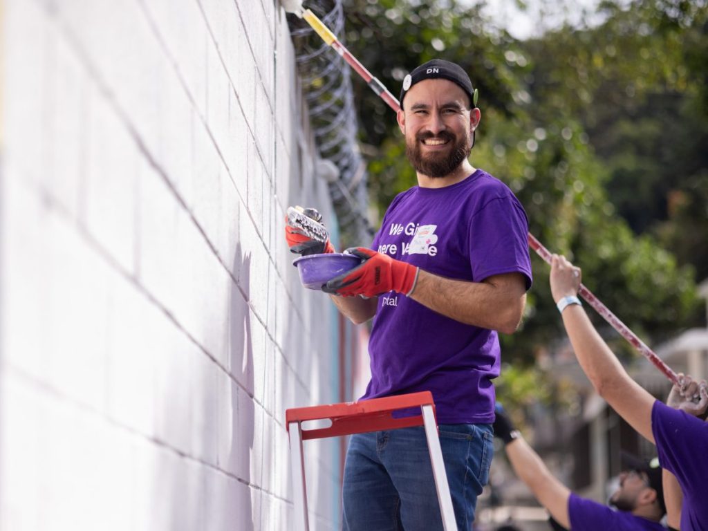 Voluntario de TELUS Digital pinta con entusiasmo un mural en el Centro Escolar Ramón Belloso, dejando color y esperanza para las futuras generaciones.