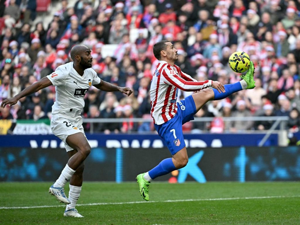 El delantero francés #07 del Atlético de Madrid, Antoine Griezmann, se prepara para marcar el segundo gol de su equipo junto al defensa francés #20 del Valencia, Dimitri Foulquier, durante el partido de la liga española entre el Club Atlético de Madrid y el Valencia CF en el Estadio Metropolitano de Madrid el 13 de diciembre de 2025. (Foto AFP)