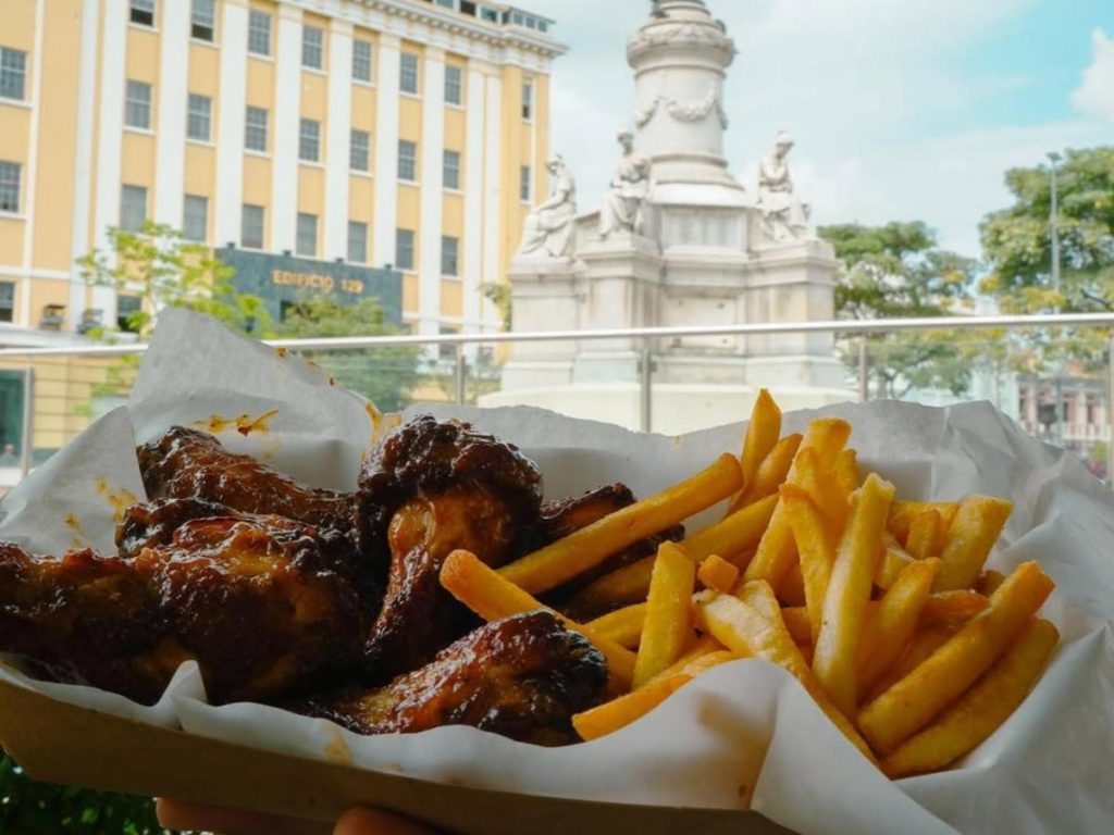 Un combo de alitas y papas de Top Burger, servido frente al icónico monumento de la Plaza Morazán, una experiencia con sabor local y vista histórica.