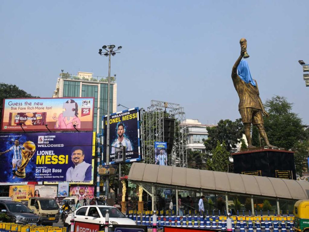 Los viajeros cruzan carteles promocionales y una estatua velada del delantero argentino número 10 del Inter de Miami, Lionel Messi, en vísperas de su visita, en Calcuta el 12 de diciembre de 2025.