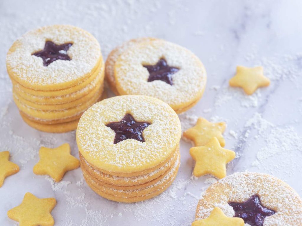 Galletas Linzer con relleno de jalea de fresa y un toque de azúcar pulverizada, perfectas para regalar o lucir en tu mesa navideña con un aire artesanal y elegante.