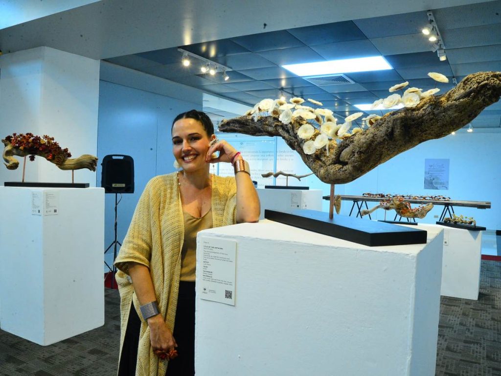 Lula Mena junto a su obra “Agradecer”, creada con tronco del mar, escamas de pescado y cobre, como símbolo de gratitud y cierre luminoso de lo vivido.