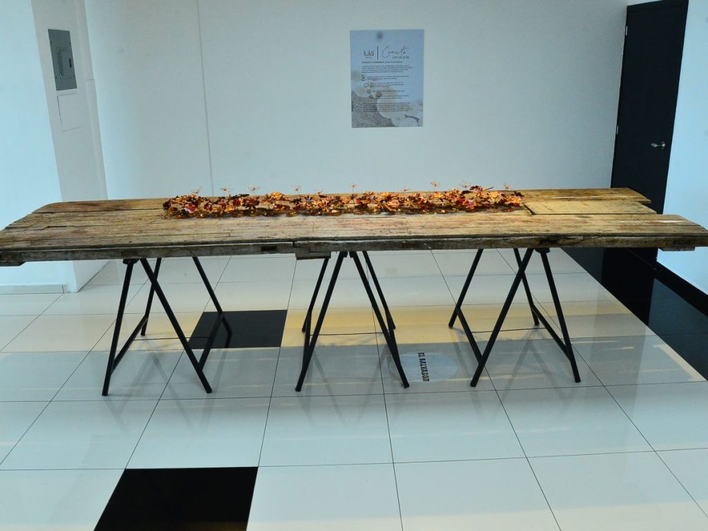 La puerta convertida en mesa es la pieza central de la muestra. Fue parte del hogar de la familia y hoy simboliza el umbral desde donde todo vuelve a florecer.