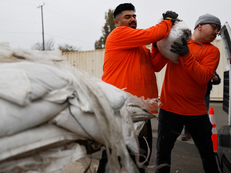 Trabajadores del condado de Los Ángeles cargan sacos de arena para un residente cerca de la zona quemada por el incendio Eaton, preparándose para una fuerte tormenta fluvial atmosférica que llegará hoy a la región el 23 de diciembre de 2025 en Altadena, California.