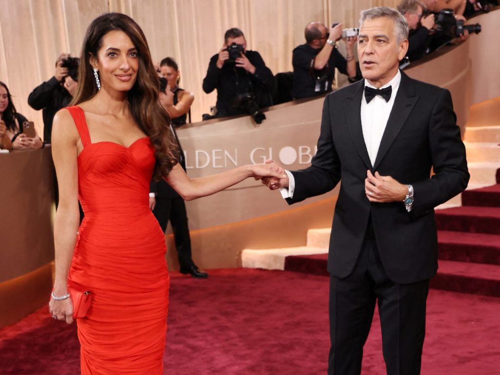 Amal Clooney posó junto a George Clooney con un vestido rojo vintage drapeado de Balmain, acompañado por joyas de Cartier y melena suelta con ondas marcadas.