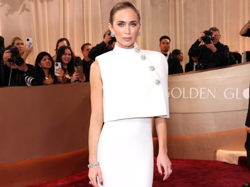 Emily Blunt eligió un vestido blanco con capa de Louis Vuitton, acompañado por joyas de Tiffany & Co. y un moño pulido con pasador-joya que completó el look.