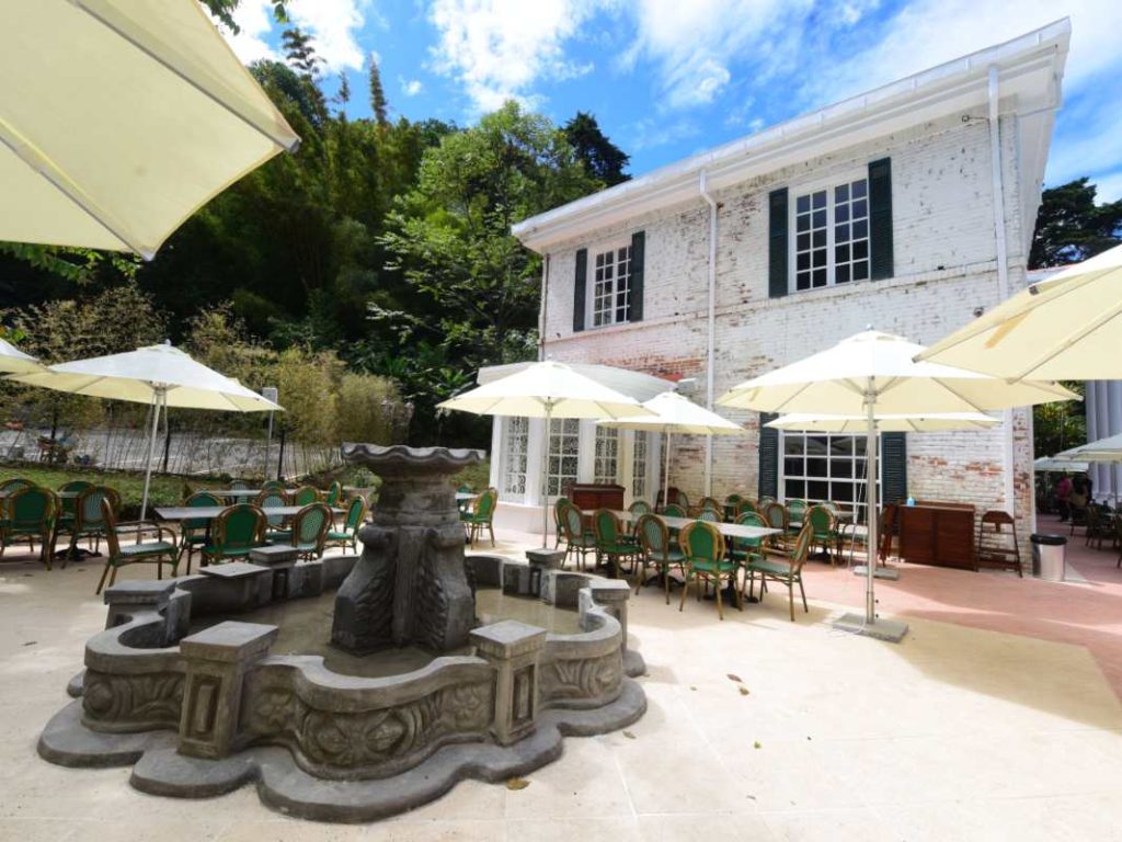 La terraza rodeada de vegetación refuerza la sensación de estar en una mansión histórica aislada del ruido urbano, en pleno Santa Tecla.