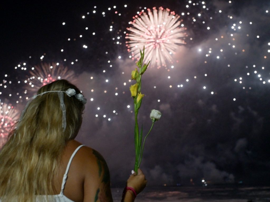 Una mujer sostiene un ramo de flores mientras celebra durante los tradicionales fuegos artificiales de Año Nuevo en la playa de Copacabana, en Río de Janeiro, Brasil, el 1de enero de 2026. Fotografía/ AFP