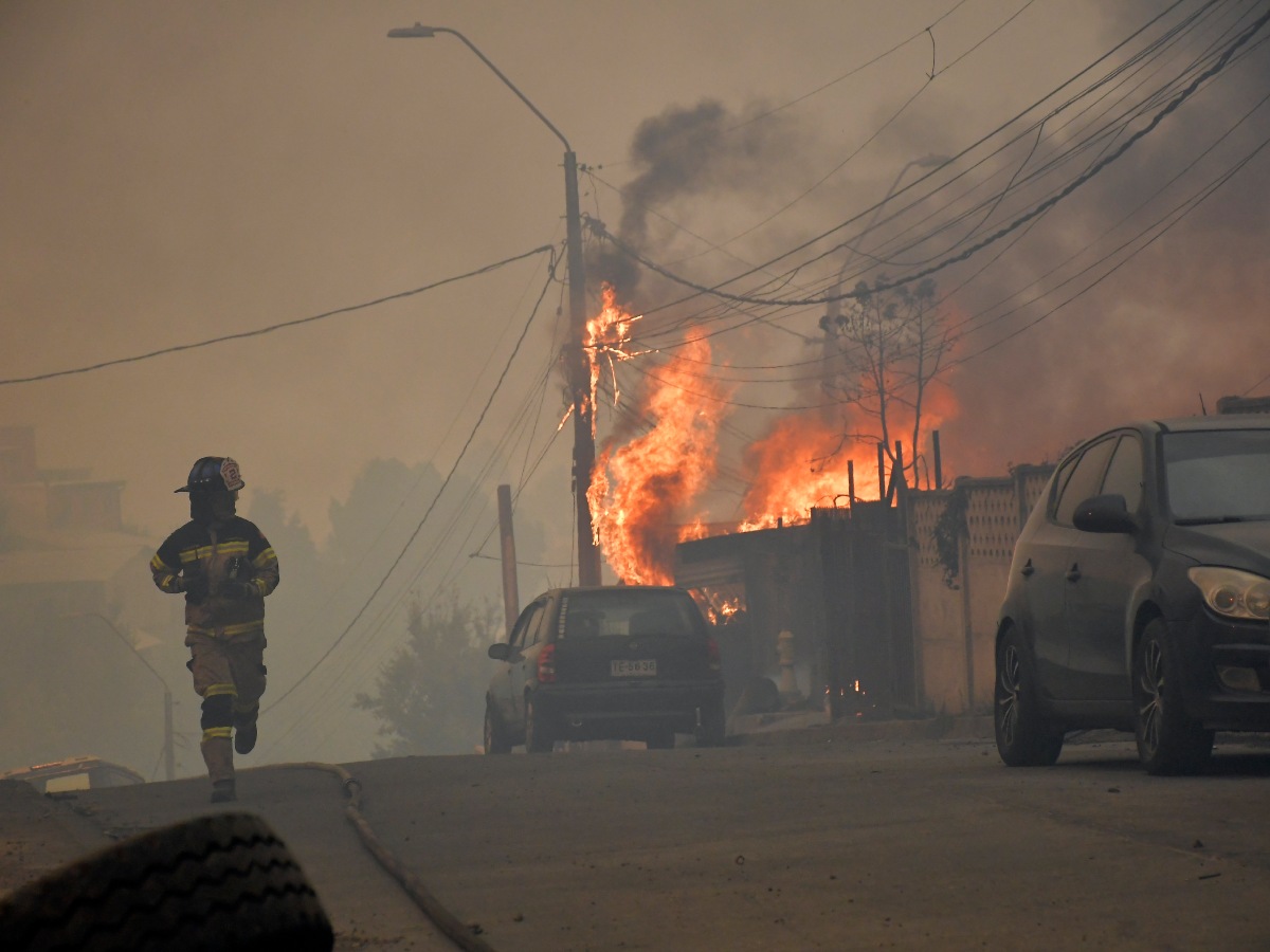 Un bombero corre por una calle mientras una vivienda arde durante un incendio forestal en Concepción, Chile, el 18 de enero de 2026.