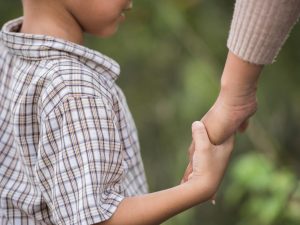 Close up of happy mum and son holding hand in a park. Family concept.