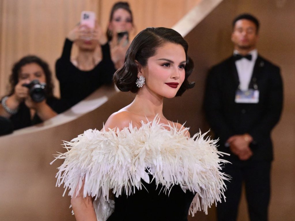 Selena Gomez eligió un vestido de terciopelo negro con plumas blancas en el escote Channel, acompañado por ondas old Hollywood, labios burdeos y pendientes Soleil Mademoiselle en oro blanco y diamantes.