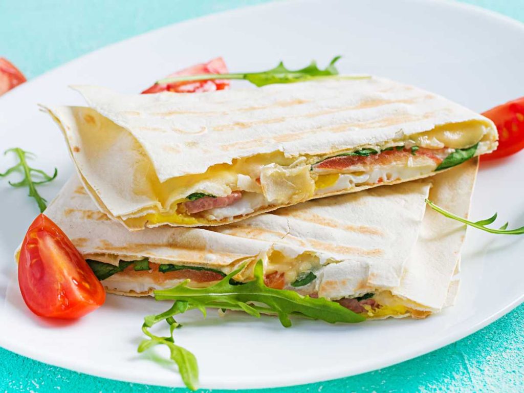 Tortillas de trigo rellenas con jamón, tomate, arúgula y queso para derretir: una opción sabrosa, fácil de llevar y perfecta para calentar al momento.