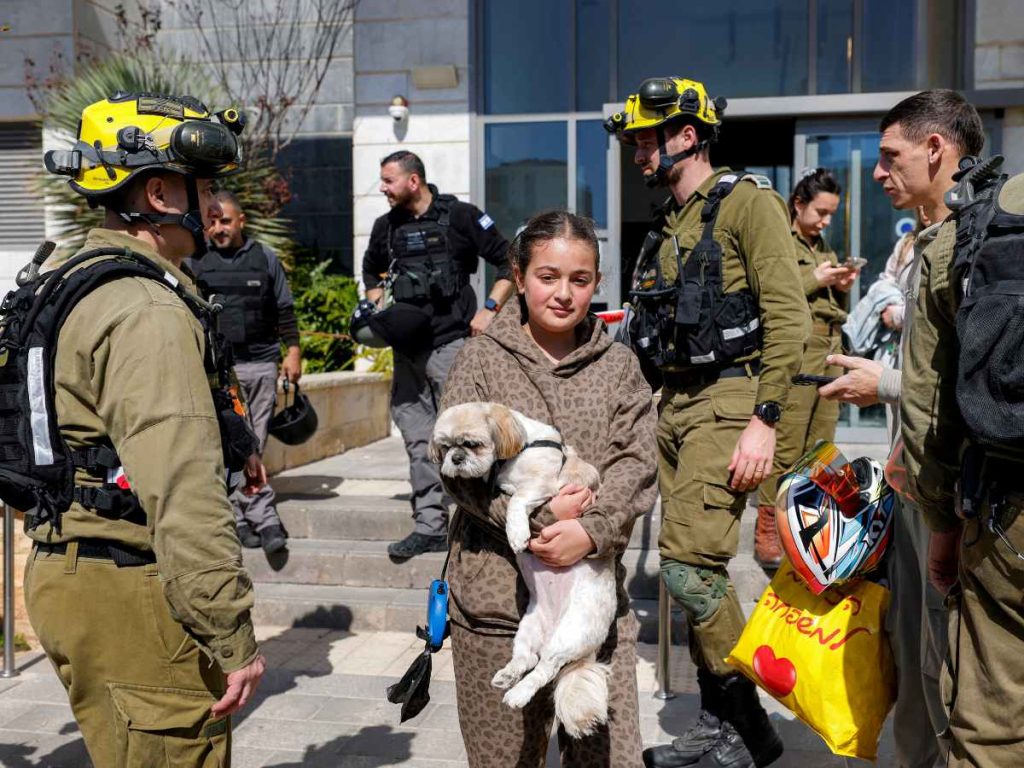 Una niña camina con un perro en la mano mientras los residentes de un edificio alcanzado por un proyectil son evacuados de las instalaciones en la ciudad de Tirat Carmel, en el norte de Israel, al sur de Haifa, el 28 de febrero de 2026.