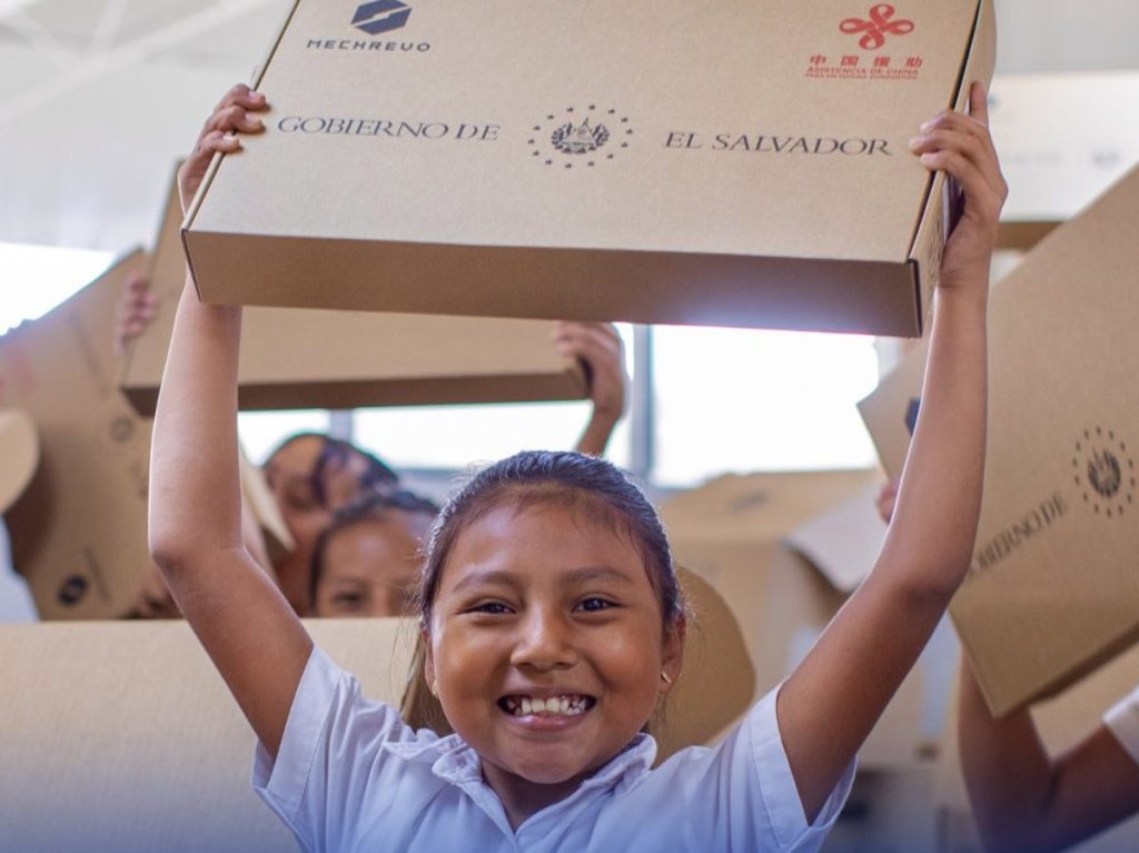 Estudiantes sostienen cajas con equipos tecnológicos que serán distribuidos en centros educativos públicos como parte del programa de apoyo escolar.