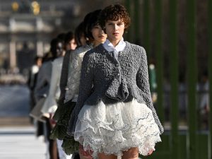 Modelo desfila para Dior en París con una silueta romántica y contemporánea: chaqueta texturizada y falda corta con capas bordadas que evocan pétalos en movimiento.