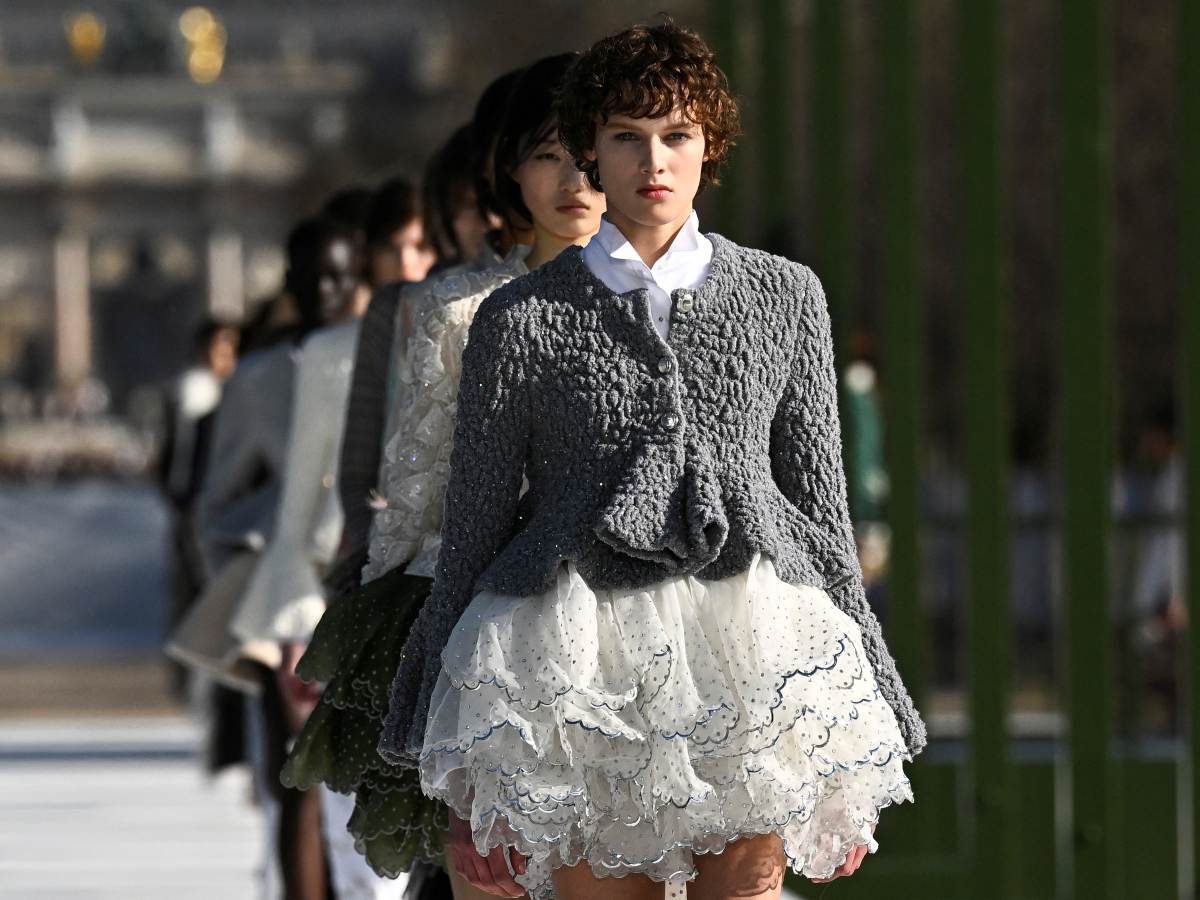 Modelo desfila para Dior en París con una silueta romántica y contemporánea: chaqueta texturizada y falda corta con capas bordadas que evocan pétalos en movimiento.
