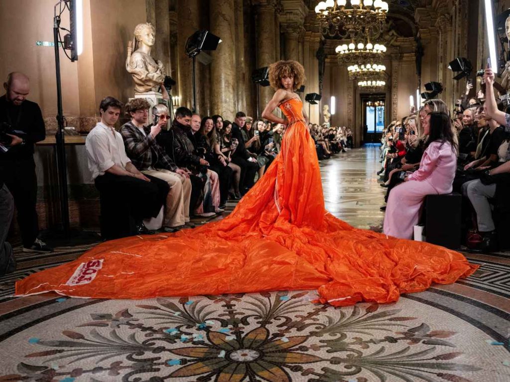 Una modelo presenta un vestido naranja con cola dramática de Max Alexander durante el desfile Otoño/Invierno 2026-2027 en la Semana de la Moda de París. 
