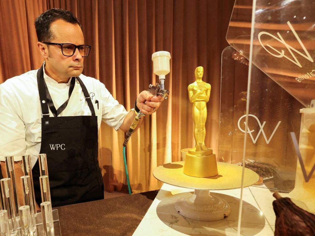 Un pastelero rocía pintura dorada sobre una estatuilla de chocolate con forma de Oscar durante la presentación del menú del Governors Ball previo a la gala.
